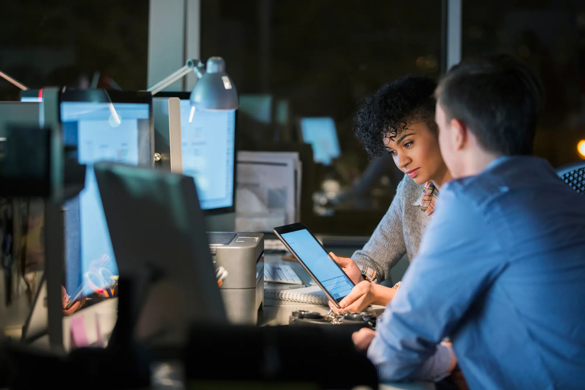 Two colleagues reviewing a product on a tablet in a late-evening office